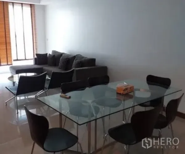 Condominium for rent in Pathum Wan, Bangkok - Open-plan lounge with glass dining table and floor-to-ceiling windows with wooden blinds.