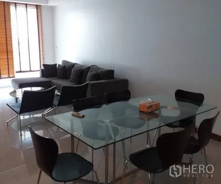 Condominium for rent in Pathum Wan, Bangkok - Open-plan lounge with glass dining table and floor-to-ceiling windows with wooden blinds.