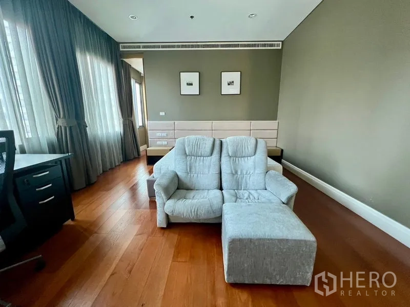 Condominium for rent in Khlong Toei, Bangkok - Large master bedroom with sofa, desk, and wraparound windows.