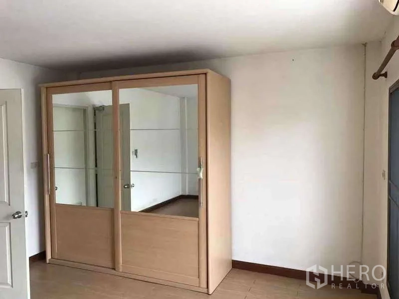 Townhouse for rent in Suan Luang, Bangkok - Bedroom with light-wood mirrored sliding wardrobe and white walls.