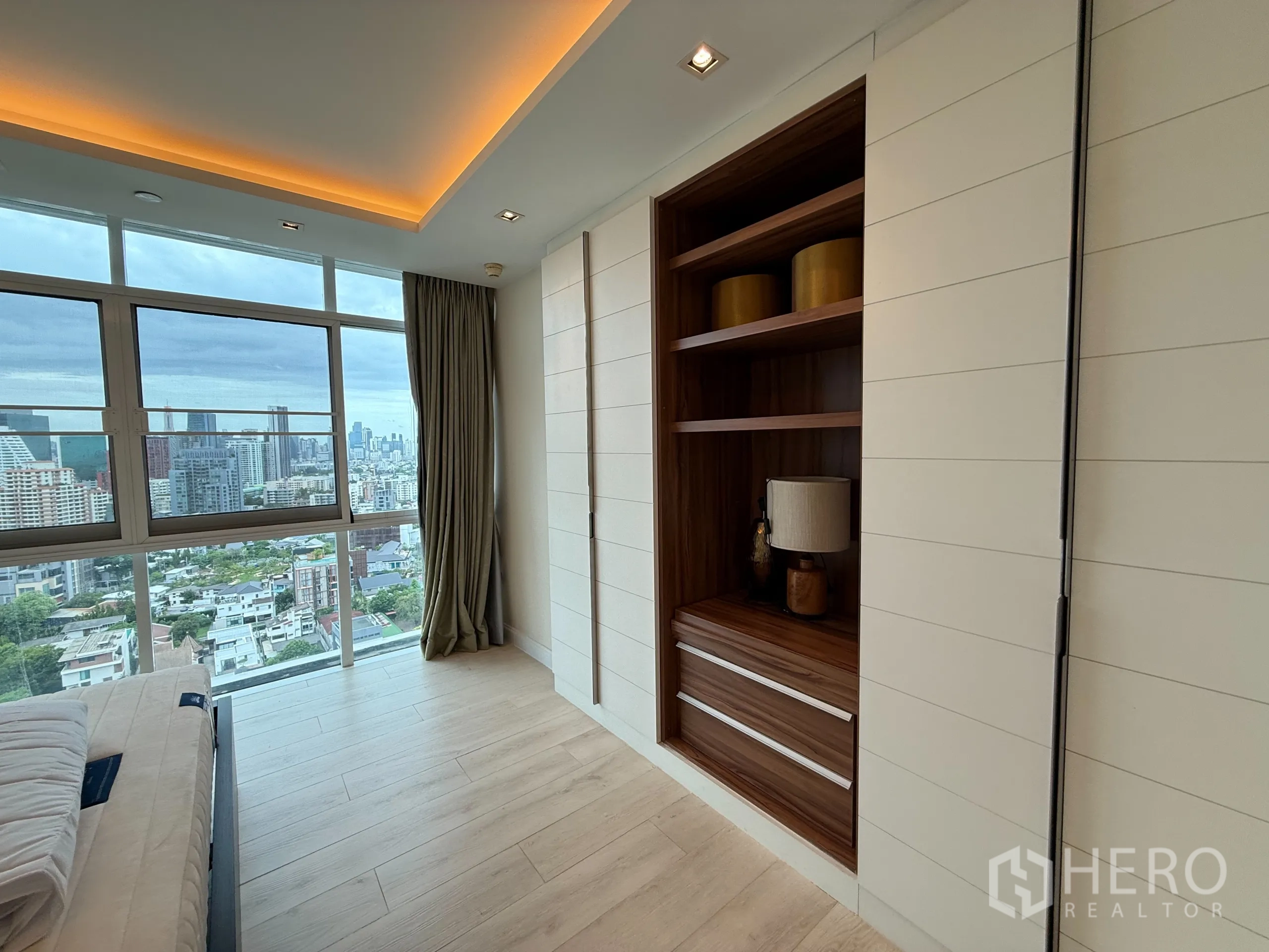 Condominium for rent in Phaya Thai, Bangkok - Bedroom with built‑in wooden shelving and wall panels beside a large city‑view window.