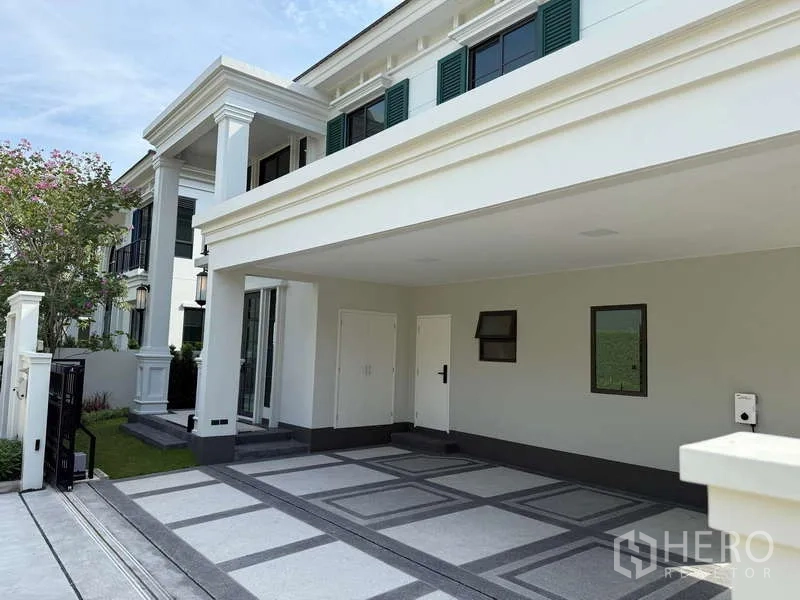 独立式住宅 出租或出售在Bang Phli, Samut Prakan - 房屋正面带有宽敞车棚与侧花园的立面。