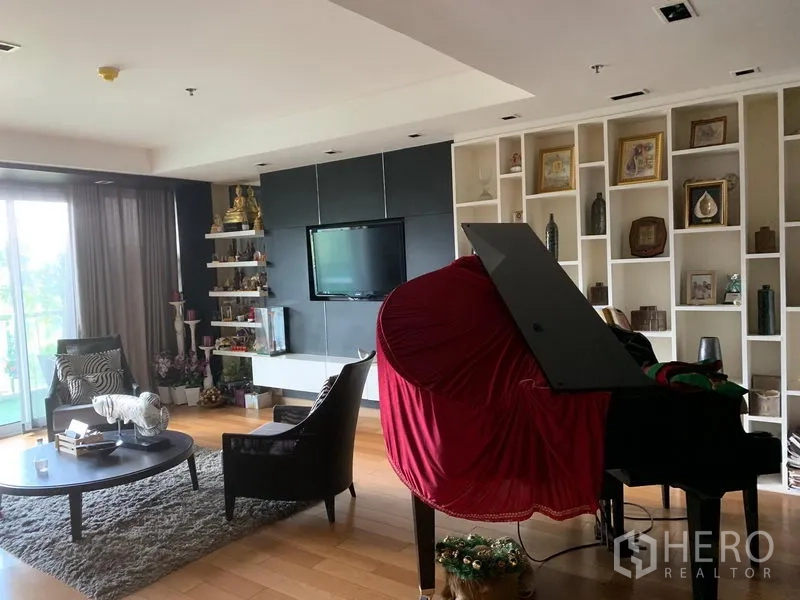 Condominium for sale in Khlong Toei, Bangkok - Lounge with built-in shelving, TV wall and a grand piano near balcony doors.