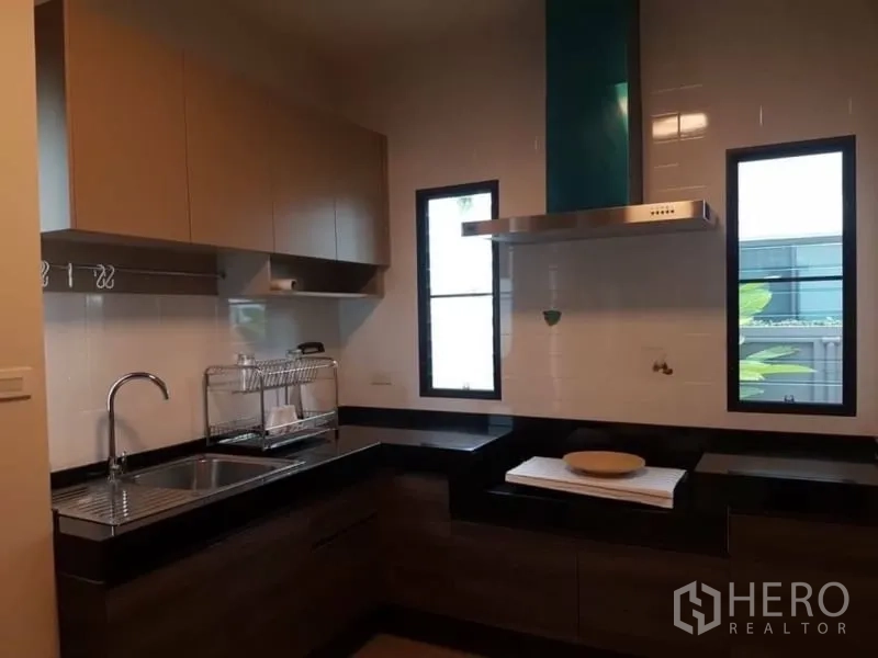 Detached House for rent in Bang Phli, Samut Prakan - Fitted L-shaped kitchen with upper cabinets, sink, cooktop and range hood between two windows.