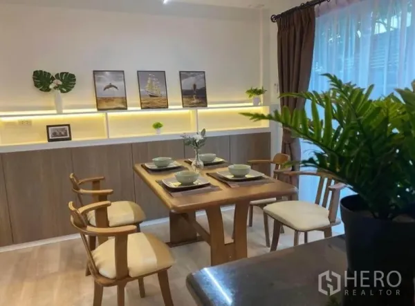 Townhouse for rent in Prawet, Bangkok - Dining area set for four with warm backlit shelving and sheer curtains.