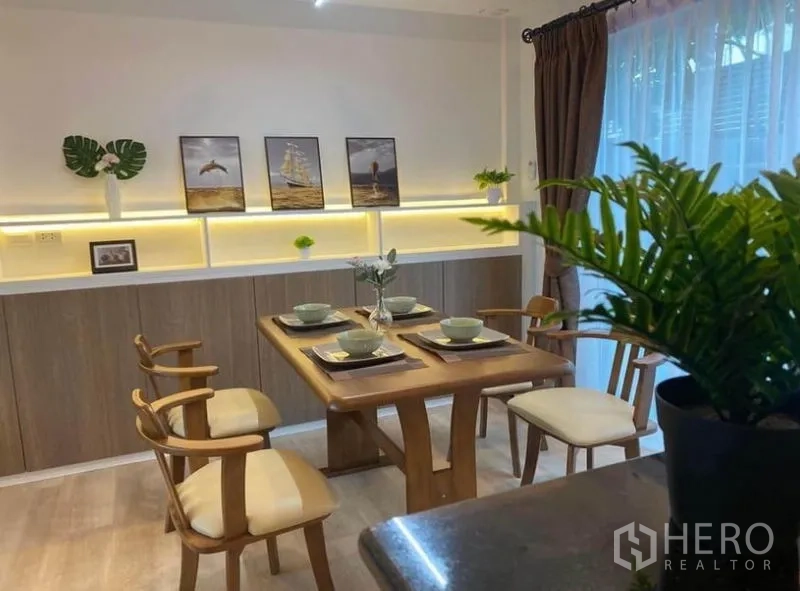 Townhouse for rent in Prawet, Bangkok - Dining area set for four with warm backlit shelving and sheer curtains.