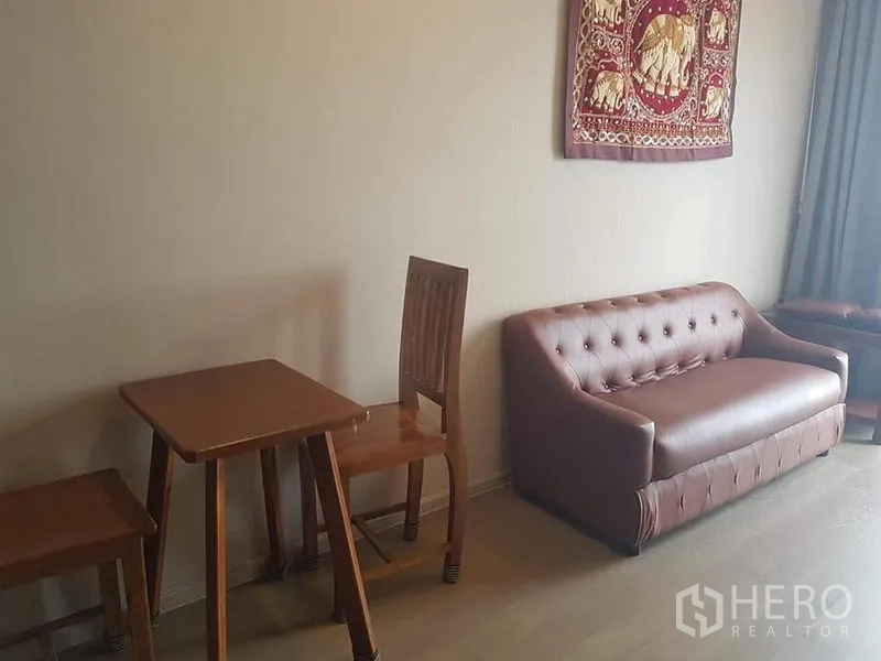 Condominium for rent in Watthana, Bangkok - Living area with brown leather sofa and small wooden dining table set.
