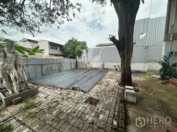 Home Office for rent in Chatuchak, Bangkok - Walled backyard with a mature tree and paved patio suitable for storage or outdoor use.