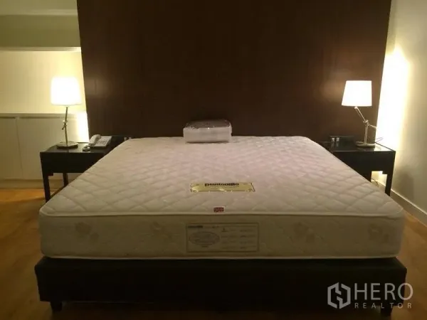 Condominium for rent in Watthana, Bangkok - Master bedroom with king-size bed, wooden accent wall, twin bedside lamps and warm lighting.