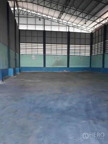Factory for rent in Samut Prakan - Large empty warehouse space with louvered wall panels and steel columns.