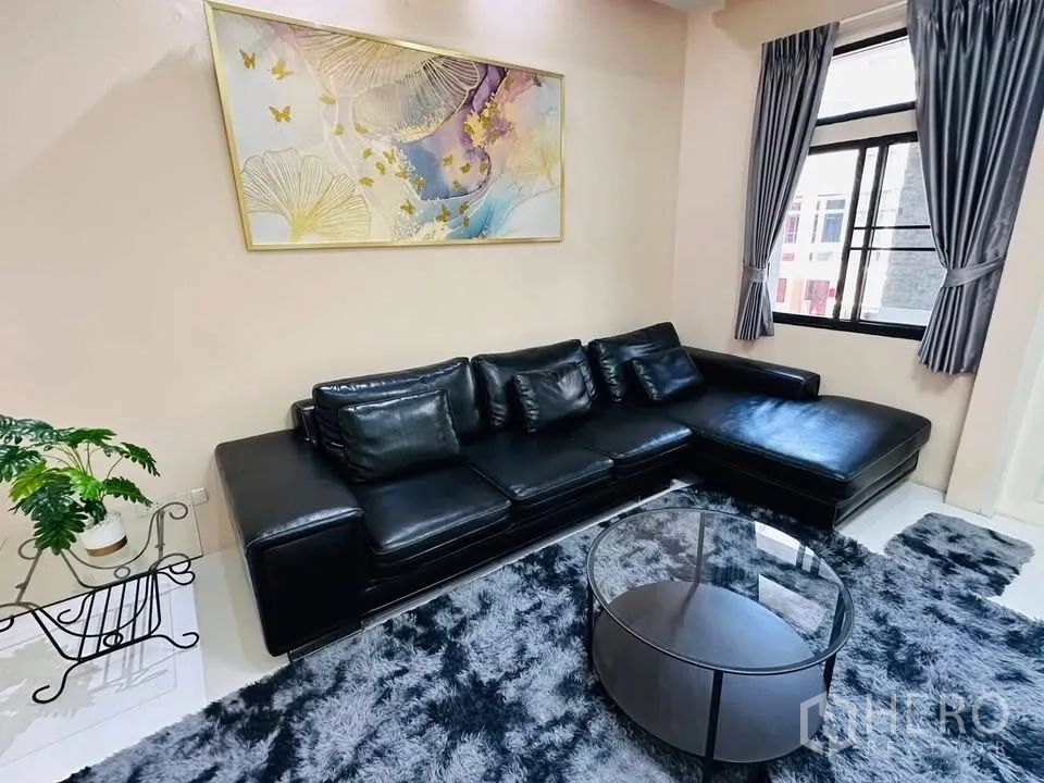 Townhouse for rent - Living room with a black L-shaped leather sofa, round glass coffee table, and plush rug.
