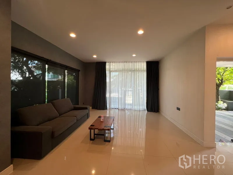 Detached House for rent or sale in Bang Kapi, Bangkok - Living room with sofa, coffee table and full-height windows opening to the garden.
