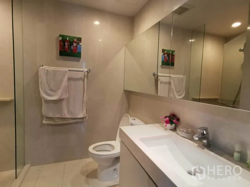 Condominium for rent in Watthana, Bangkok - Guest bathroom with glass shower enclosure, toilet and wide vanity with mirror.