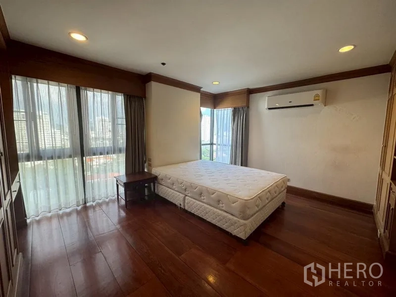 Condominium for rent in Watthana, Bangkok - Master bedroom with large windows, wood floors, and air conditioning.