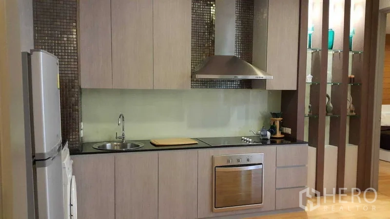Condominium for rent in Khlong Toei, Bangkok - Built-in kitchen with oven, cooktop, hood, sink and a glass backsplash.