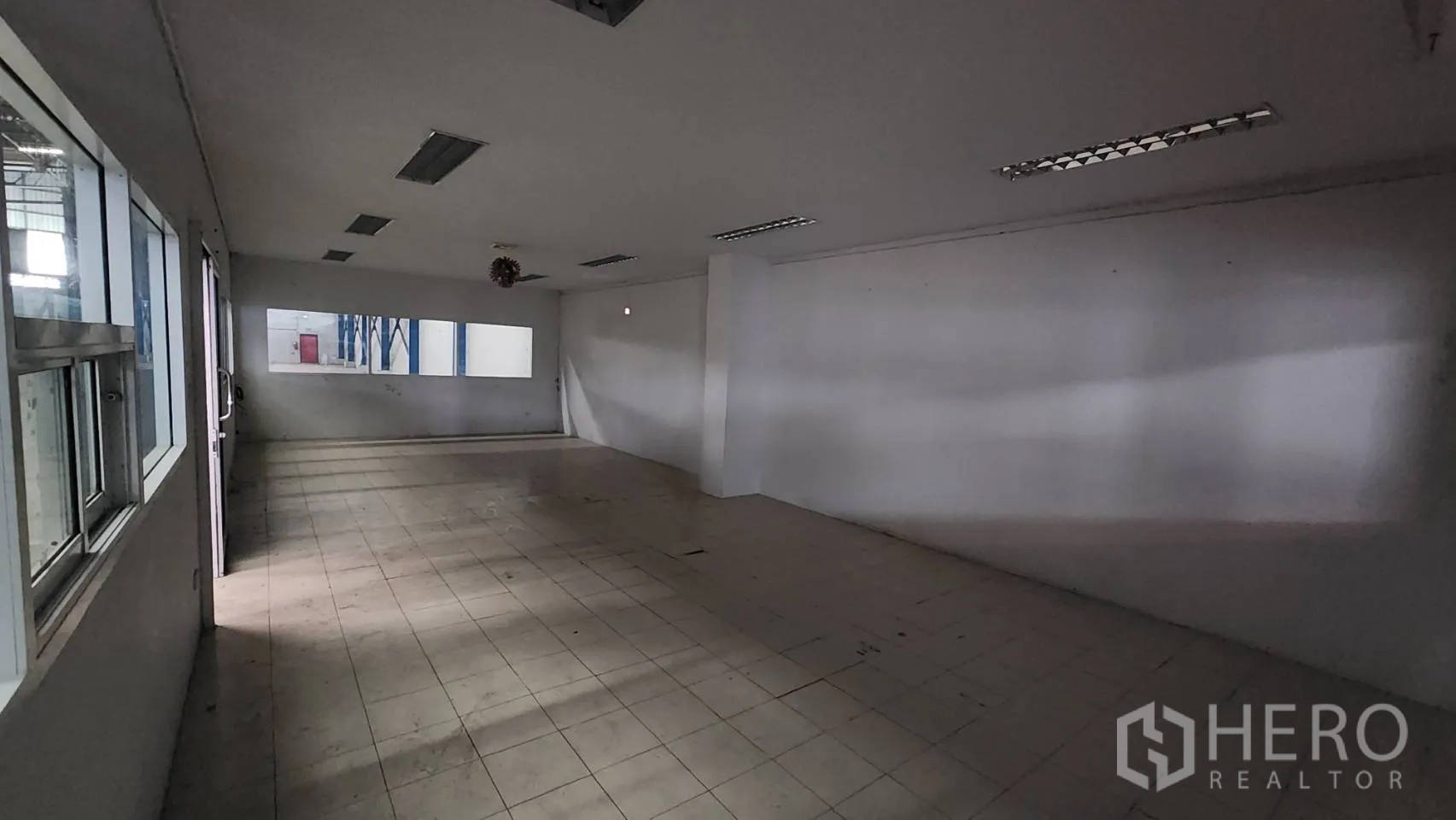 Warehouse for rent in Mueang Samut Prakan, Samut Prakan - Large tiled office room with fluorescent lighting and windows overlooking the warehouse floor.