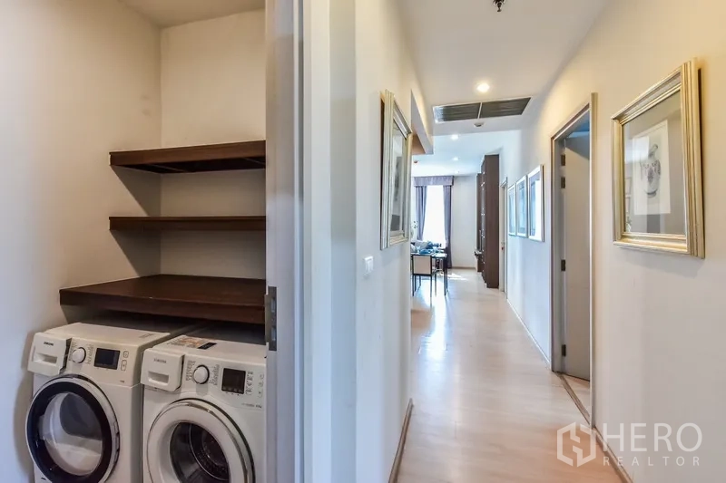 Condominium for rent or sale in Huai Khwang, Bangkok - Laundry nook in the hallway with washer, dryer, and storage shelves.