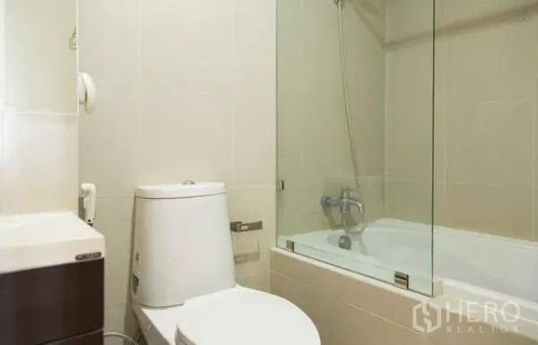 Condominium for rent in Khlong Toei, Bangkok - Modern bathroom with bathtub-shower combo behind a glass screen and a compact toilet.