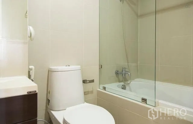Condominium for rent in Khlong Toei, Bangkok - Modern bathroom with bathtub-shower combo behind a glass screen and a compact toilet.