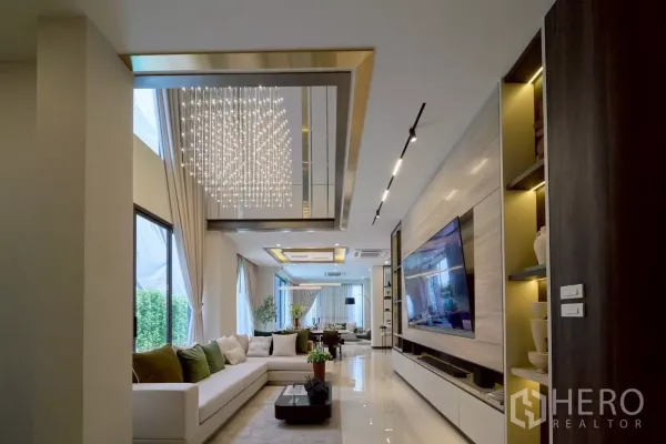 Detached House for sale in Lat Phrao, Bangkok - Open-plan living room with L-shaped sofa, large TV wall and sparkling crystal chandelier.