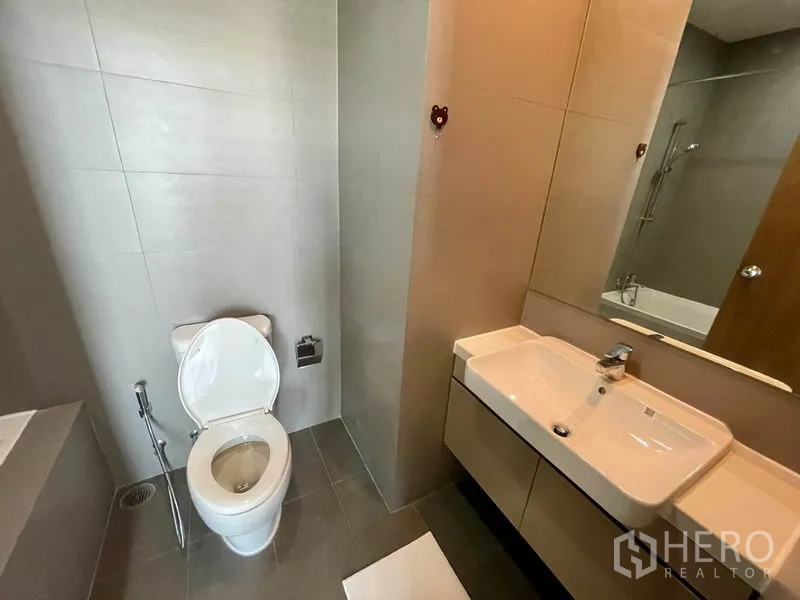 Condominium for rent in Phaya Thai, Bangkok - Bathroom vanity with large mirror and sink cabinet next to toilet and tub.