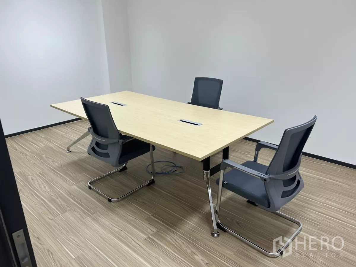 Office Space for rent - Compact meeting room with a rectangular table and three chairs on wood floors and clean white walls.