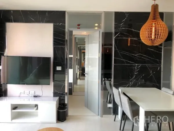 Condominium for rent in Khlong Toei, Bangkok - Open-plan lounge with wall-mounted TV, black marble feature wall, and a four-seat dining table.