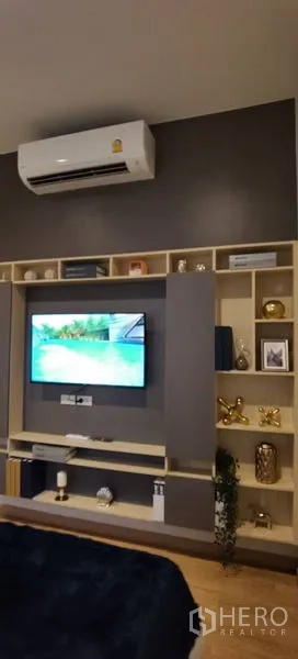 联排别墅 出租在Prawet, Bangkok - 起居区电视与开放置物架一体化，空调位于上方。