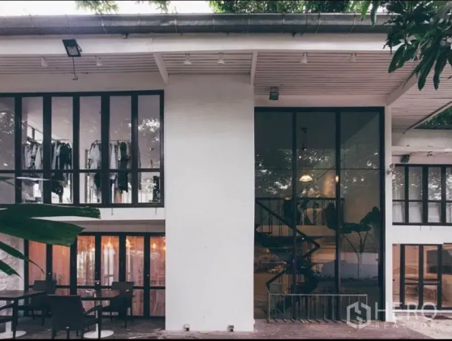 Retail Space for rent in Khlong Toei, Bangkok - Modern two‑storey retail building with floor‑to‑ceiling windows, a visible spiral staircase and outdoor seating shaded by trees.