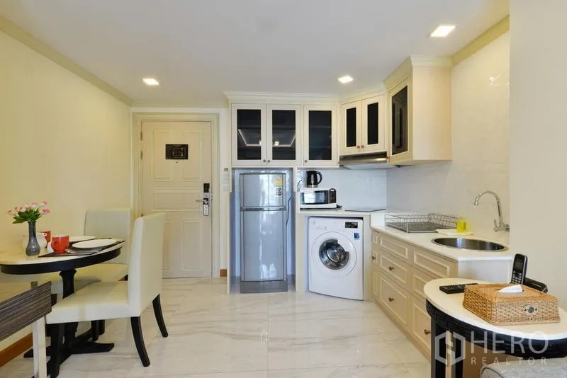 Apartment for rent in Khlong Toei, Bangkok - Compact kitchen with white cabinetry, fridge, washing machine, microwave, and dining set.