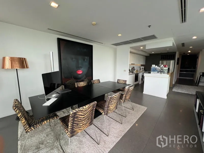 Condominium for sale in Khlong San, Bangkok - Dining area with long black table, animal-print chairs, and connected open kitchen.