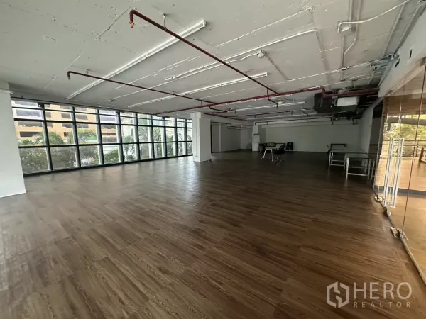 Retail Space for rent - Open-plan retail floor with floor-to-ceiling windows and exposed ceiling piping.