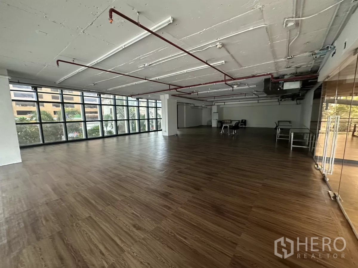 Retail Space for rent - Open-plan retail floor with floor-to-ceiling windows and exposed ceiling piping.