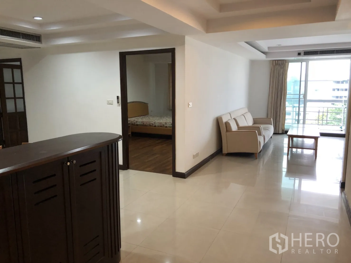 Condominium for rent in Watthana, Bangkok - Living space with cream sofa and balcony access via sliding doors.