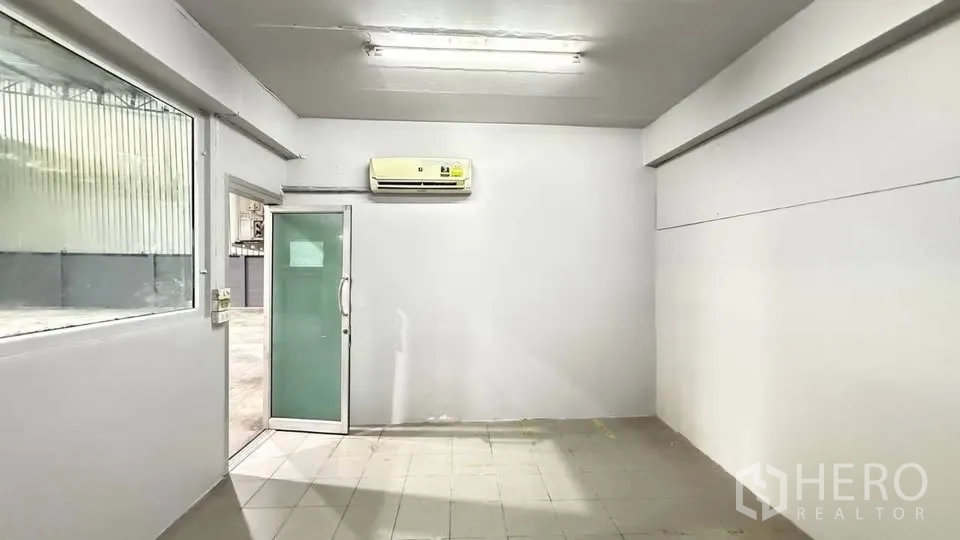 Warehouse for rent in Bang Na, Bangkok - Small internal office with glass door, window and wall-mounted air conditioner.
