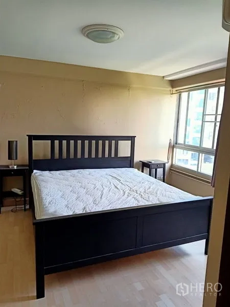 Condominium for rent in Khlong Toei, Bangkok - Master bedroom with queen bed, side tables and a bright corner window.