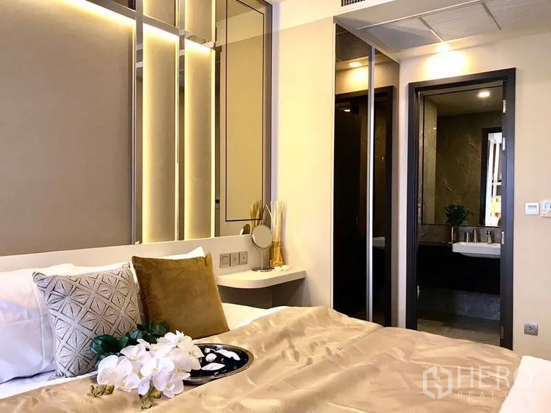 คอนโด ให้เช่าในWatthana, Bangkok - ห้องนอนโทนอบอุ่น หัวเตียงบุซอฟท์พาเนล กระจกเงา และประตูเชื่อมห้องน้ำลายหินอ่อน
