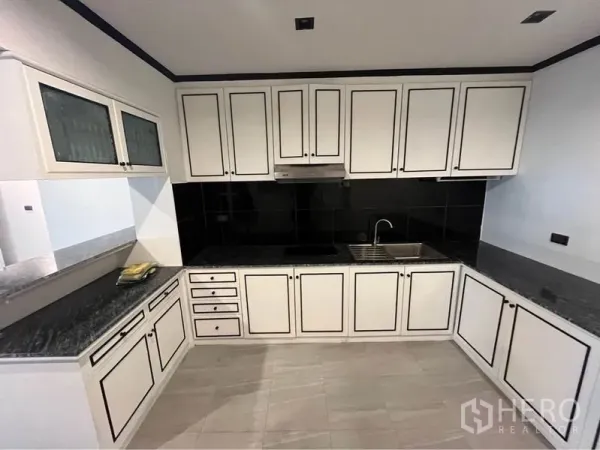 Condominium for rent or sale in Watthana, Bangkok - U-shaped kitchen with white paneled cabinets, black backsplash and granite counters.