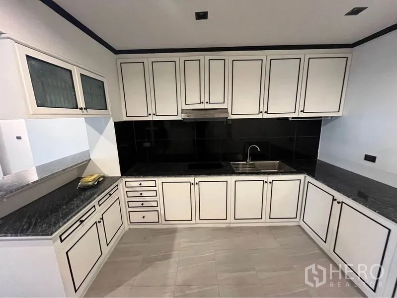 Condominium for rent or sale in Watthana, Bangkok - U-shaped kitchen with white paneled cabinets, black backsplash and granite counters.
