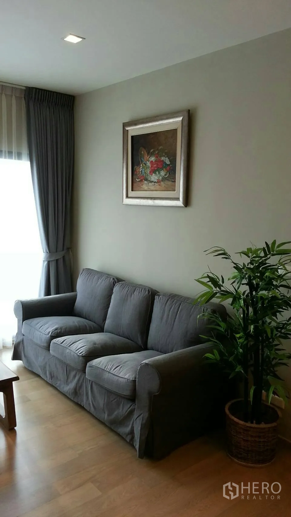 Condominium for rent or sale in Watthana, Bangkok - Cozy living room with gray sofa, large window with curtains and a potted plant.