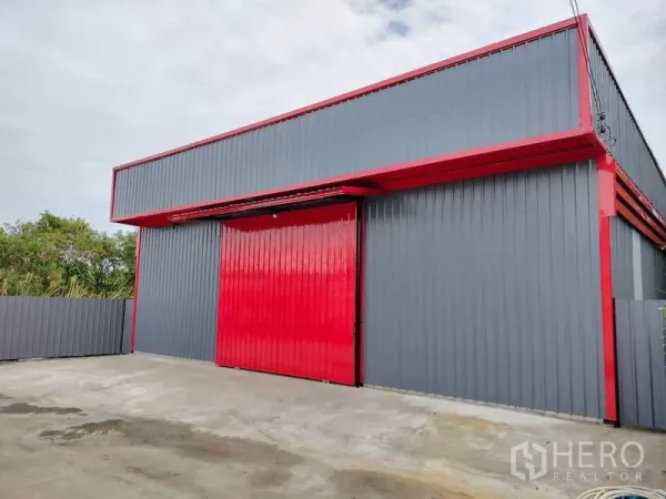 Warehouse for rent in Bueng Kum, Bangkok - Front facade of grey warehouse with bold red door and driveway for truck access.