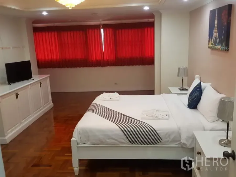 公寓 出租在Watthana, Bangkok - 宽敞卧室，白色床铺，内置电视柜，拼花木地板与红色窗帘。