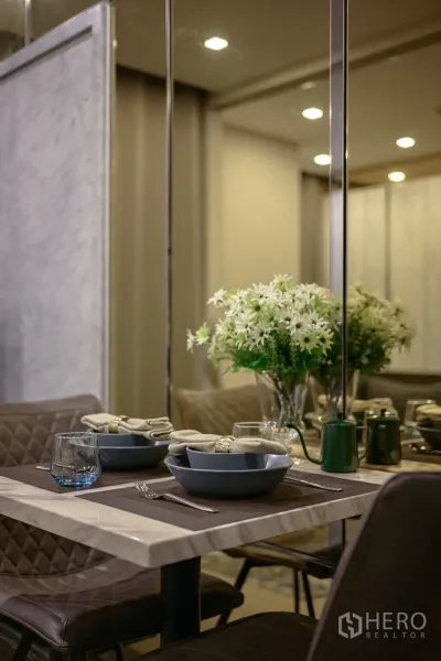Condominium for rent in Watthana, Bangkok - Marble dining table set for two with flowers beside a mirrored wall.