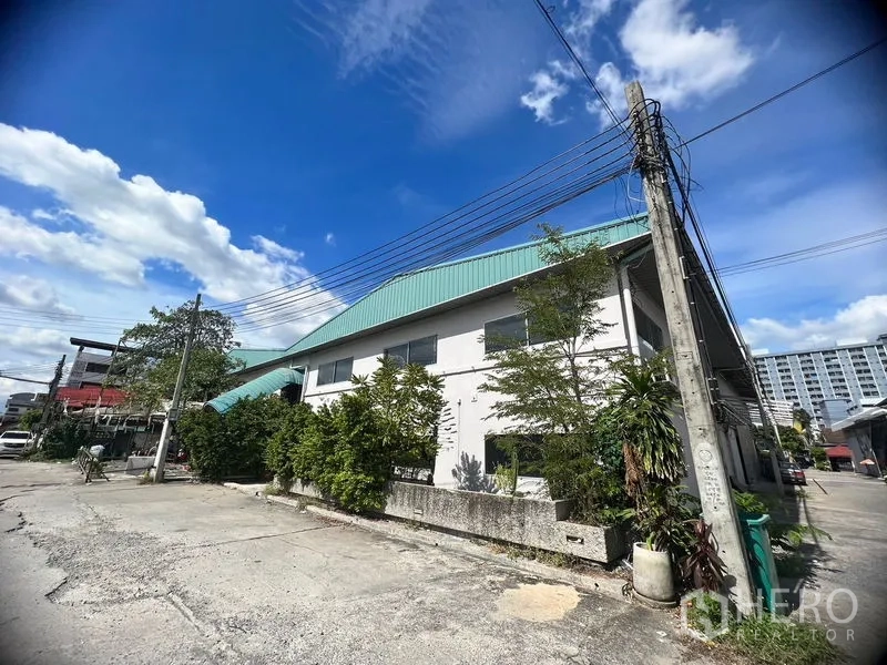 Warehouse for rent in Suan Luang, Bangkok - Corner view of the warehouse building on a side street with greenery and nearby condos.