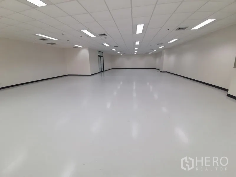 Office Space for rent in Bang Rak, Bangkok - Symmetrical view of a bright unfurnished office under a grid ceiling with fluorescent lights.