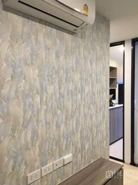 公寓 出售在Bang Na, Bangkok - 柔蓝纹理背景墙、电源插座与空调，靠近厨房入口。