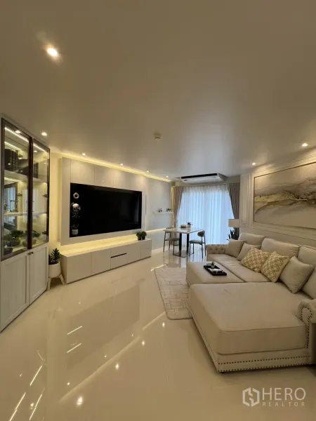 Condominium for rent in Yan Nawa, Bangkok - Elegant living room with large sectional sofa, TV wall unit, and sheer curtains by the window.