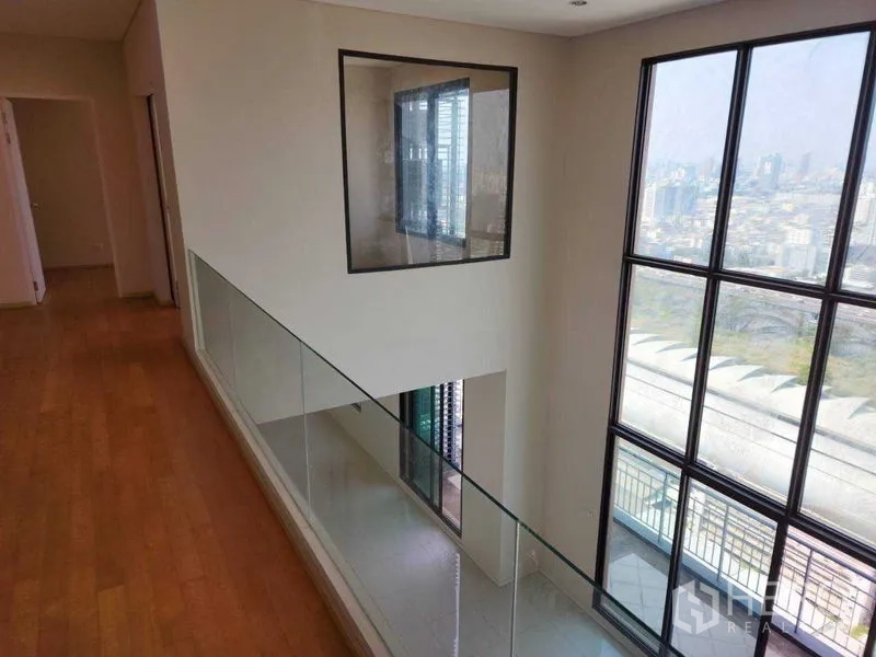 公寓 出租在Ratchathewi, Bangkok - 夹层走廊配玻璃栏杆，俯瞰挑高落地窗与城市天际线。