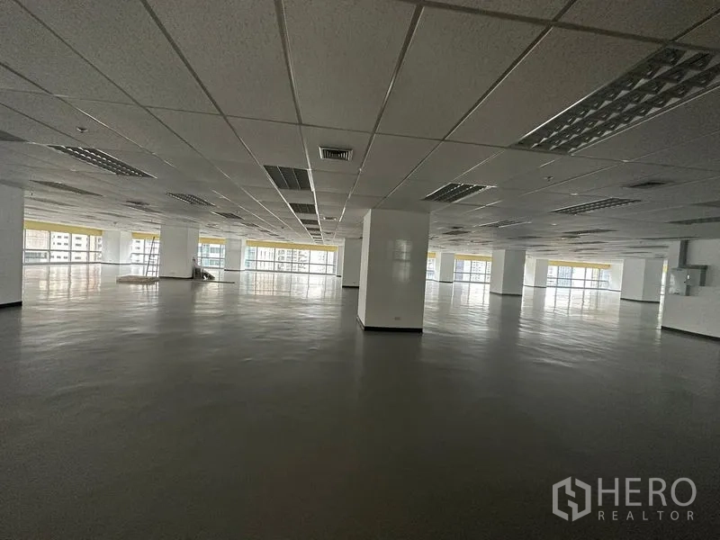 办公空间 出租 - 宽敞的开放式办公室楼层，吊顶、承重柱与大面积落地窗，可欣赏城市景观。