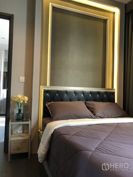 公寓 出租在Watthana, Bangkok - 优雅卧室，软包床头与暖色氛围灯，床头柜摆放鲜花。